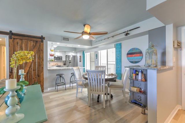 dining area with ceiling fan, a barn door, and light hardwood / wood-style floors