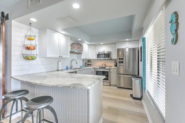 kitchen featuring backsplash, white cabinets, appliances with stainless steel finishes, and light hardwood / wood-style flooring