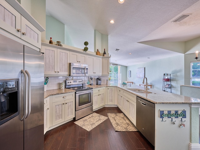 kitchen with a textured ceiling, sink, kitchen peninsula, stainless steel appliances, and dark hardwood / wood-style flooring