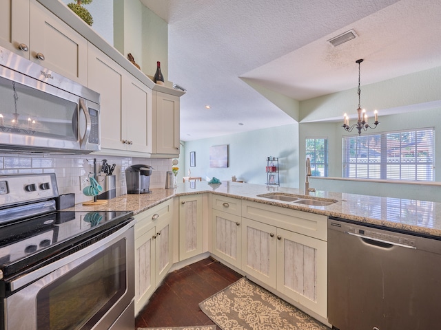 kitchen with light stone counters, sink, kitchen peninsula, dark wood-type flooring, and appliances with stainless steel finishes