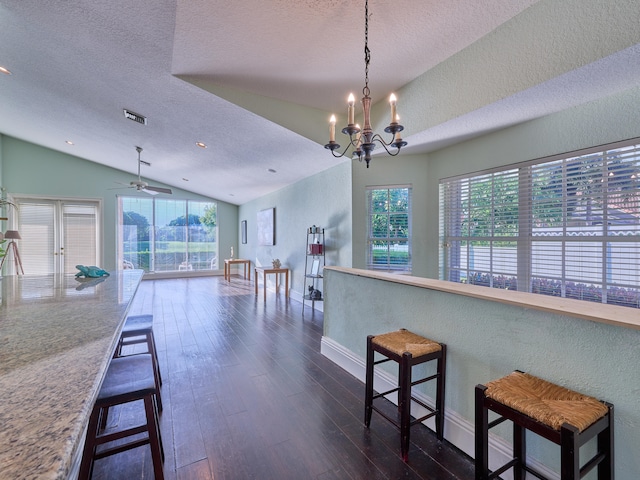 kitchen featuring vaulted ceiling, dark wood-type flooring, a textured ceiling, a kitchen bar, and decorative light fixtures