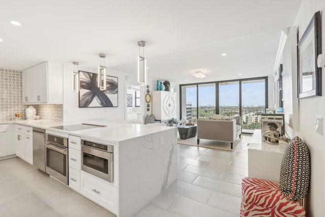 kitchen with pendant lighting, backsplash, white cabinets, expansive windows, and appliances with stainless steel finishes