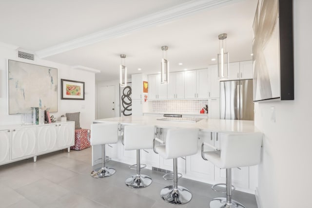 kitchen featuring kitchen peninsula, stainless steel fridge, a breakfast bar, white cabinetry, and hanging light fixtures