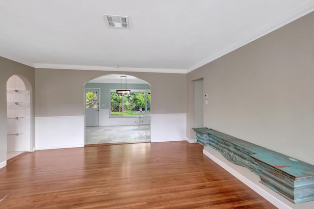 unfurnished room featuring crown molding, arched walkways, visible vents, and wood finished floors