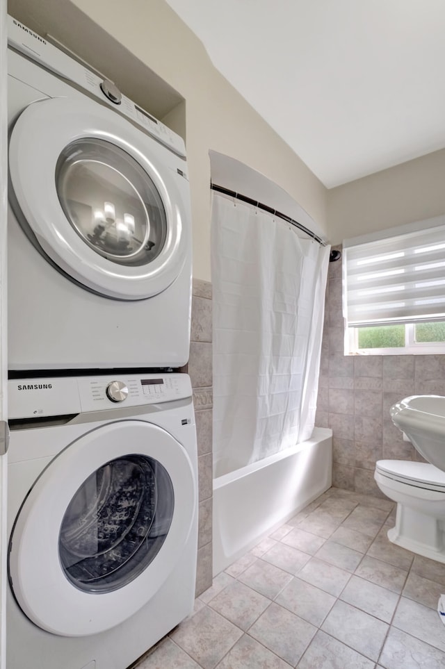 laundry room featuring light tile patterned floors, tile walls, and stacked washer and dryer