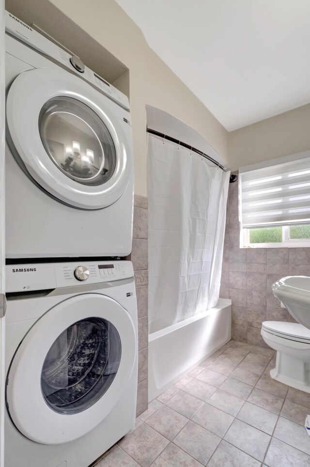 interior space with tile patterned floors, shower / bathtub combination with curtain, stacked washer / drying machine, and toilet