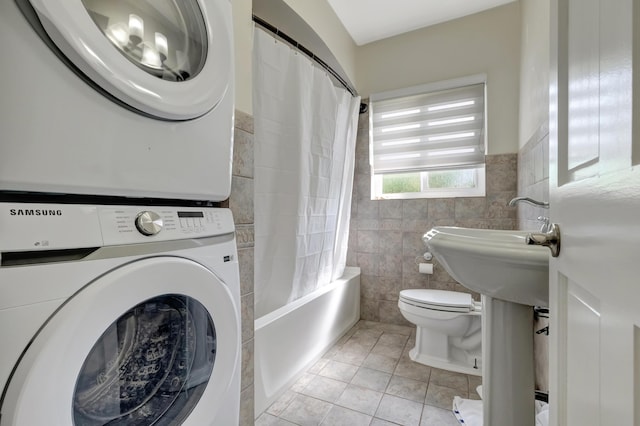 full bathroom featuring tile patterned flooring, stacked washer / dryer, toilet, tile walls, and a wainscoted wall
