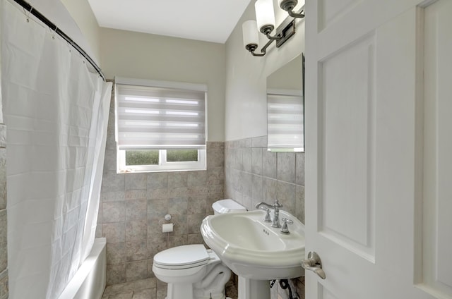 bathroom with a sink, toilet, shower / bathtub combination with curtain, a wainscoted wall, and tile walls