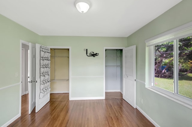 unfurnished bedroom with baseboards, wood finished floors, multiple windows, and two closets