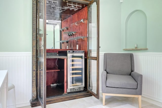 interior space with wine cooler, a bar, and wainscoting