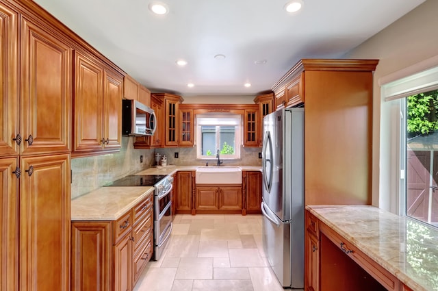 kitchen featuring backsplash, appliances with stainless steel finishes, sink, and light stone counters