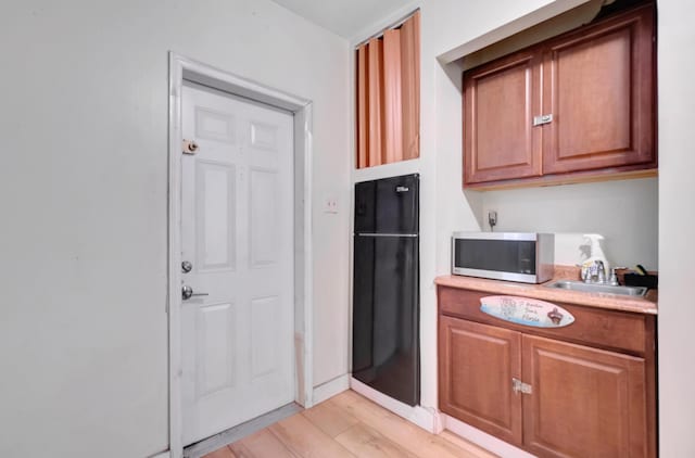 kitchen with light countertops, stainless steel microwave, brown cabinets, a sink, and light wood-style flooring