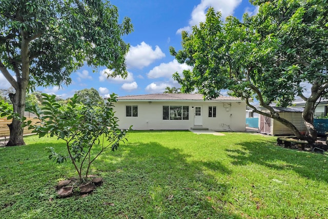 rear view of house with a lawn, a storage shed, a tile roof, and stucco siding