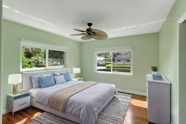 bedroom featuring baseboards, multiple windows, a ceiling fan, and wood finished floors