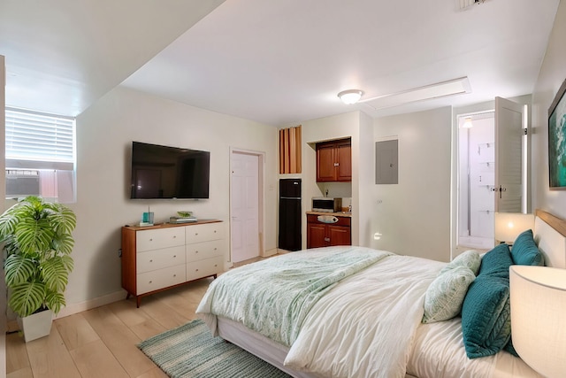 bedroom featuring electric panel, light wood-type flooring, and black refrigerator