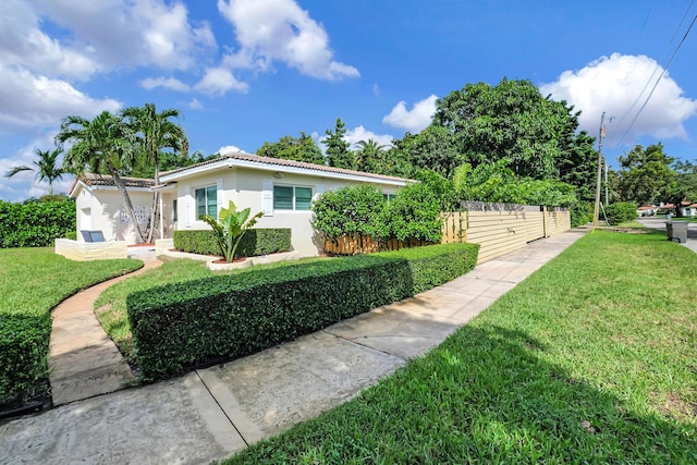 view of side of property featuring a lawn, stucco siding, a tiled roof, and fence