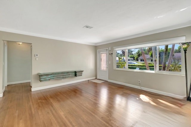 unfurnished living room featuring crown molding, baseboards, wood finished floors, and visible vents