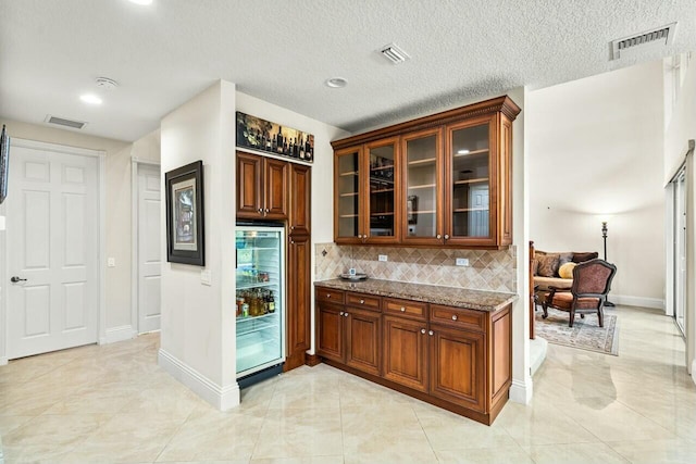 kitchen featuring tasteful backsplash, light stone countertops, black appliances, a kitchen island, and beverage cooler