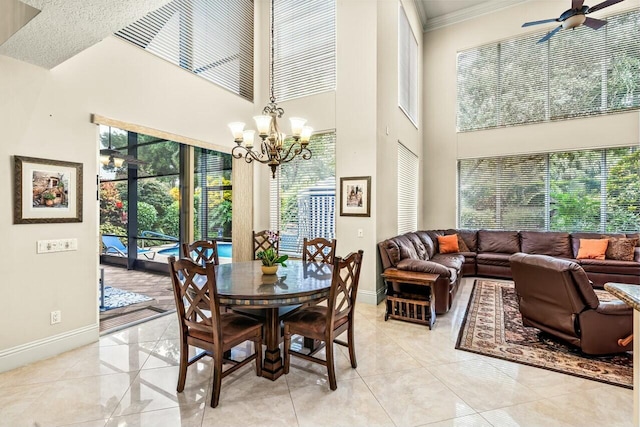 tiled dining area featuring a high ceiling, ornamental molding, and ceiling fan with notable chandelier