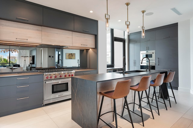 kitchen featuring sink, a kitchen bar, designer stove, a kitchen island with sink, and pendant lighting