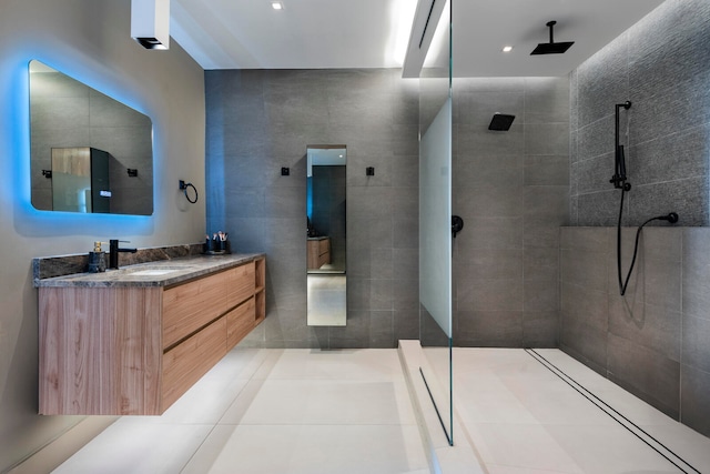 bathroom with tile walls, tile patterned flooring, vanity, and a shower