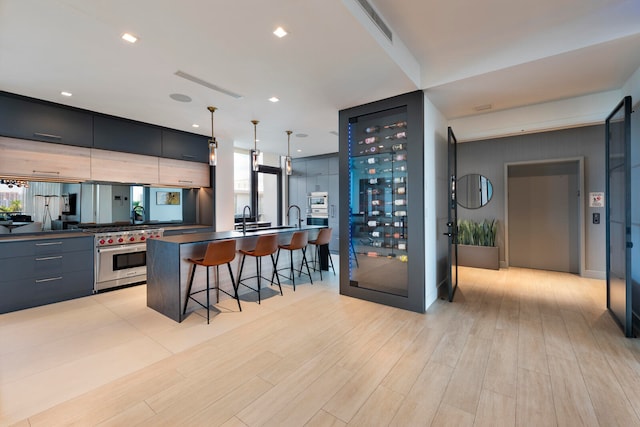 kitchen featuring a kitchen bar, hanging light fixtures, premium stove, light wood-type flooring, and a large island with sink