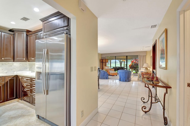 kitchen with decorative backsplash, dark brown cabinetry, light tile patterned flooring, and stainless steel fridge