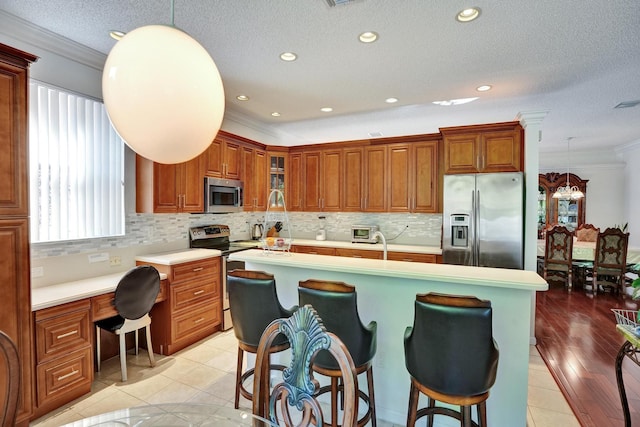 kitchen with pendant lighting, light tile patterned flooring, an island with sink, ornamental molding, and appliances with stainless steel finishes