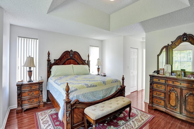 bedroom with a textured ceiling, dark wood-type flooring, and multiple windows