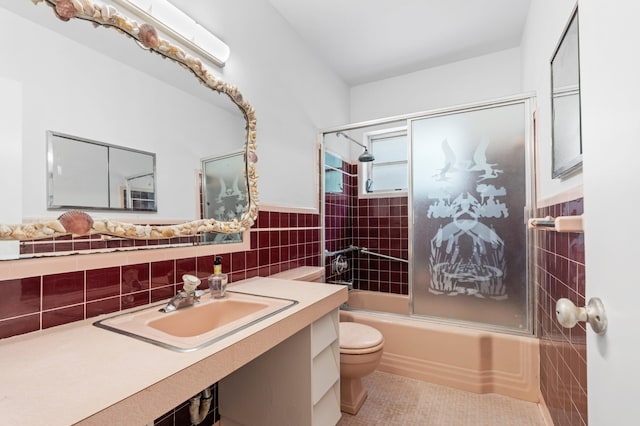 bathroom featuring shower / bath combination with glass door, toilet, tile walls, tile patterned flooring, and wainscoting