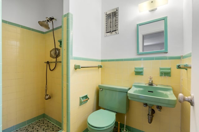 bathroom with tile walls, a sink, tiled shower, toilet, and wainscoting