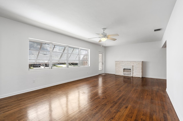 unfurnished living room with a stone fireplace, dark wood-type flooring, and ceiling fan