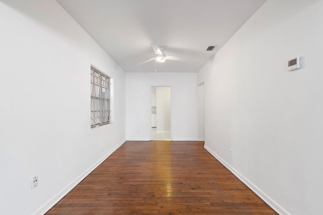 empty room with visible vents, a ceiling fan, dark wood finished floors, and baseboards