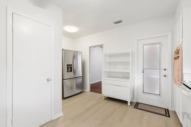 kitchen with stainless steel fridge, white cabinets, light wood finished floors, baseboards, and visible vents