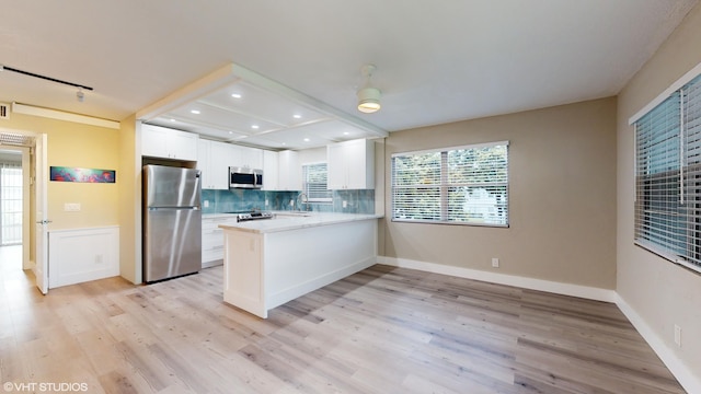 kitchen with white cabinets, kitchen peninsula, light hardwood / wood-style flooring, backsplash, and appliances with stainless steel finishes