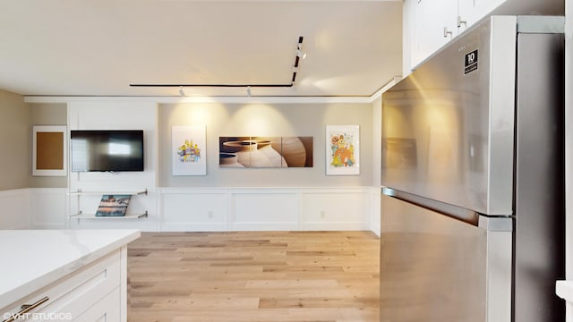 kitchen with light stone counters, white cabinets, stainless steel refrigerator, and light hardwood / wood-style flooring