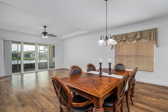 dining space with crown molding, a water view, a tray ceiling, dark hardwood / wood-style flooring, and ceiling fan with notable chandelier