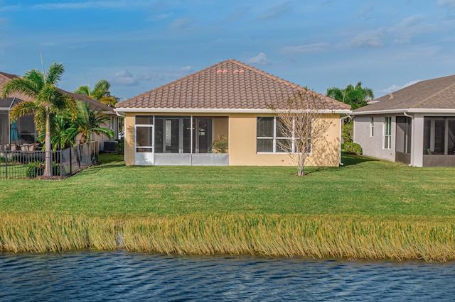 back of property with a water view, a sunroom, and a lawn