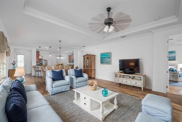 living room featuring dark hardwood / wood-style flooring, ceiling fan with notable chandelier, and ornamental molding