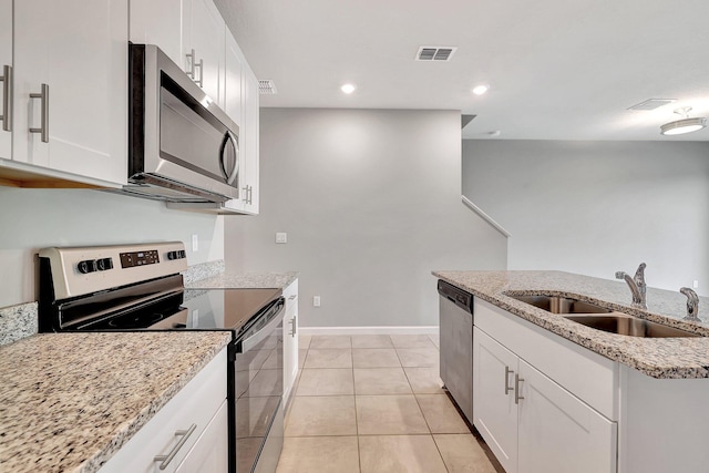 kitchen featuring sink, light stone countertops, white cabinets, light tile patterned floors, and appliances with stainless steel finishes