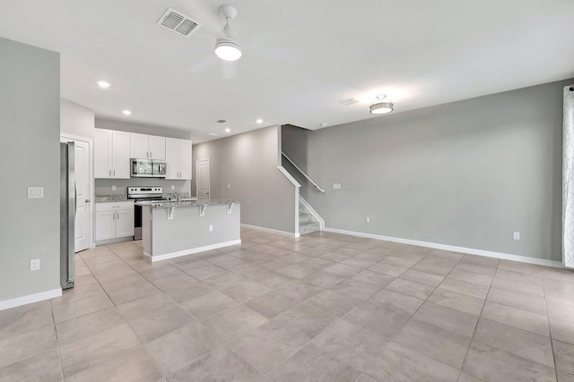 kitchen featuring a breakfast bar area, stainless steel appliances, a center island with sink, white cabinetry, and light stone counters