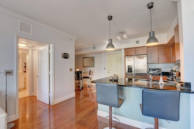 kitchen with pendant lighting, hardwood / wood-style floors, kitchen peninsula, and stainless steel fridge with ice dispenser