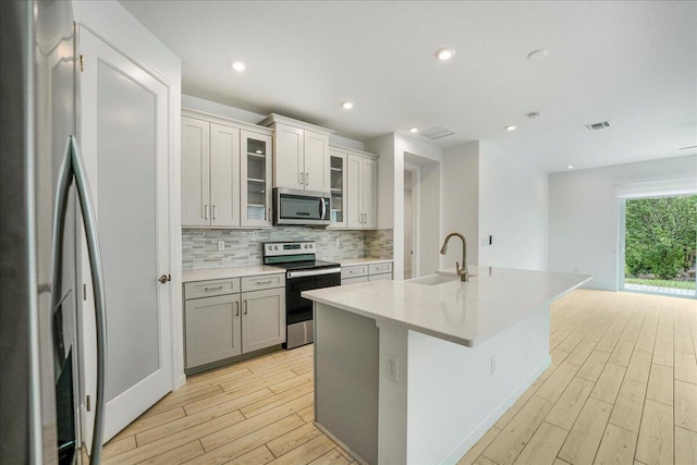 kitchen featuring light hardwood / wood-style floors, appliances with stainless steel finishes, a kitchen island with sink, and sink