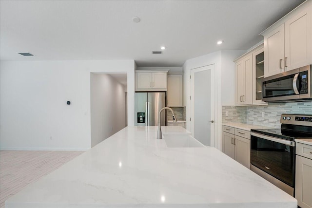 kitchen featuring light wood-type flooring, sink, tasteful backsplash, stainless steel appliances, and light stone countertops