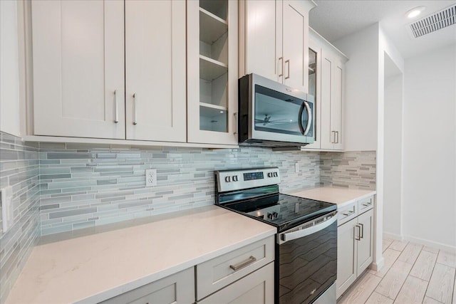 kitchen featuring decorative backsplash, stainless steel appliances, white cabinetry, and light hardwood / wood-style floors