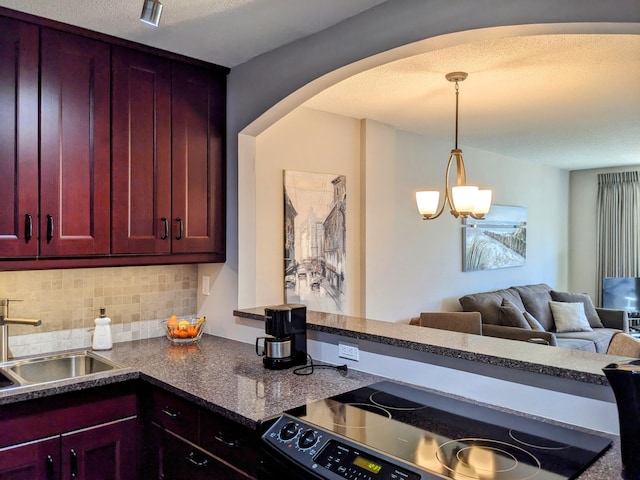 kitchen featuring tasteful backsplash, black range, sink, pendant lighting, and a notable chandelier