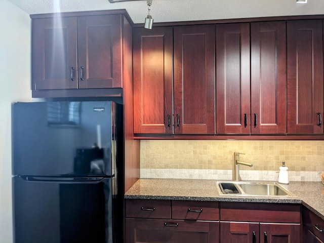 kitchen with decorative backsplash, sink, stone counters, and refrigerator