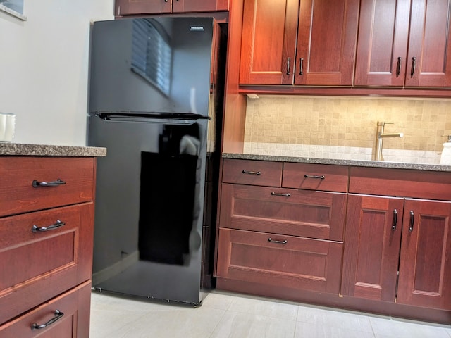 kitchen with decorative backsplash, light stone countertops, light tile patterned flooring, and black fridge