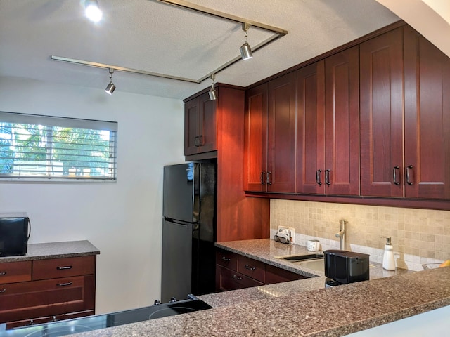 kitchen with track lighting, dark stone counters, tasteful backsplash, and black fridge