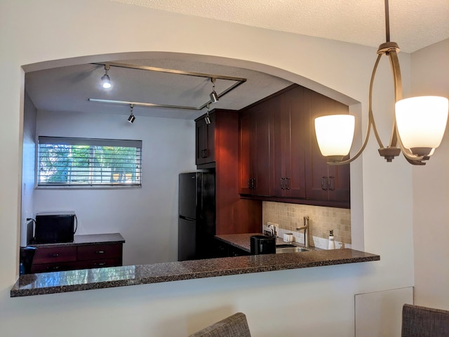 kitchen featuring track lighting, black fridge, pendant lighting, a textured ceiling, and tasteful backsplash